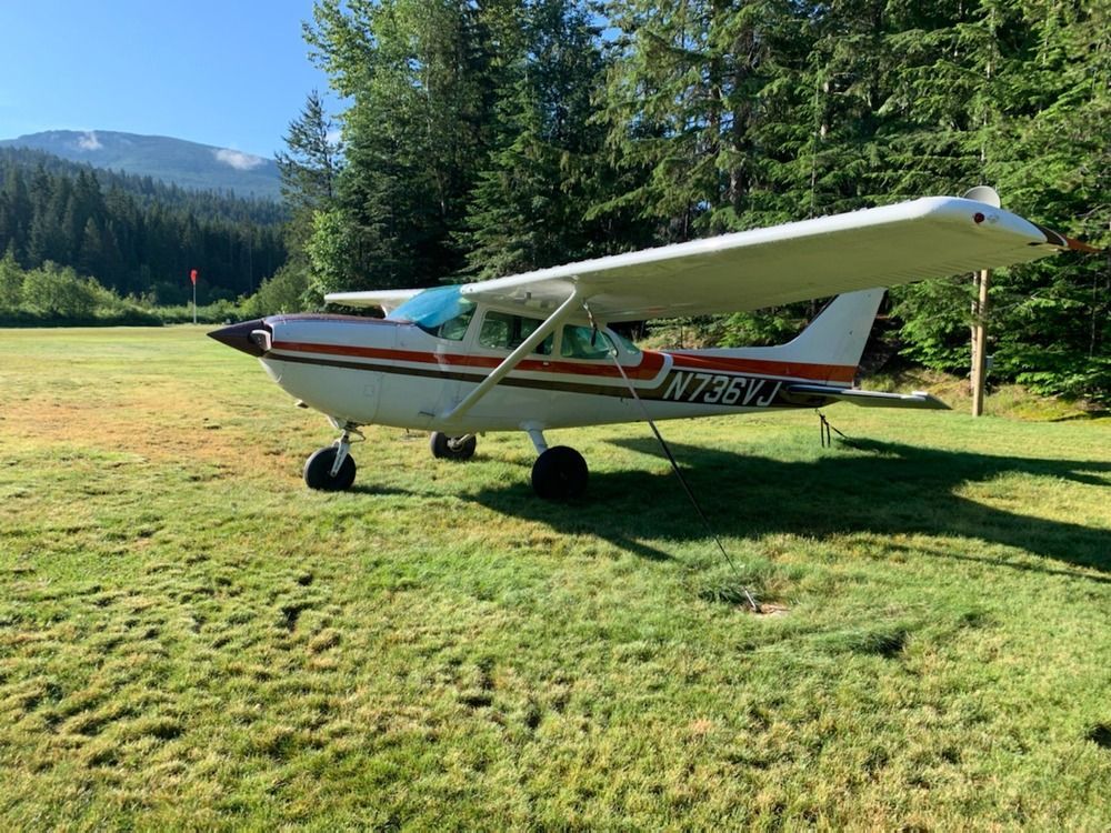 A small plane is parked in a grassy field with mountains in the background.