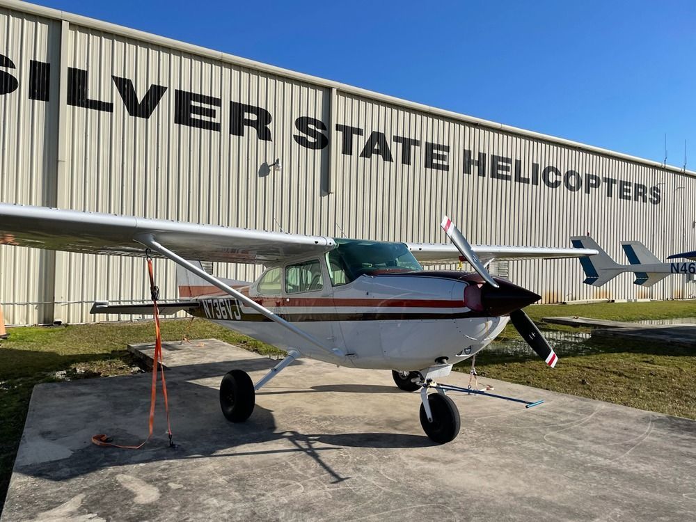 A small plane is parked in front of a building that says silver state helicopters.