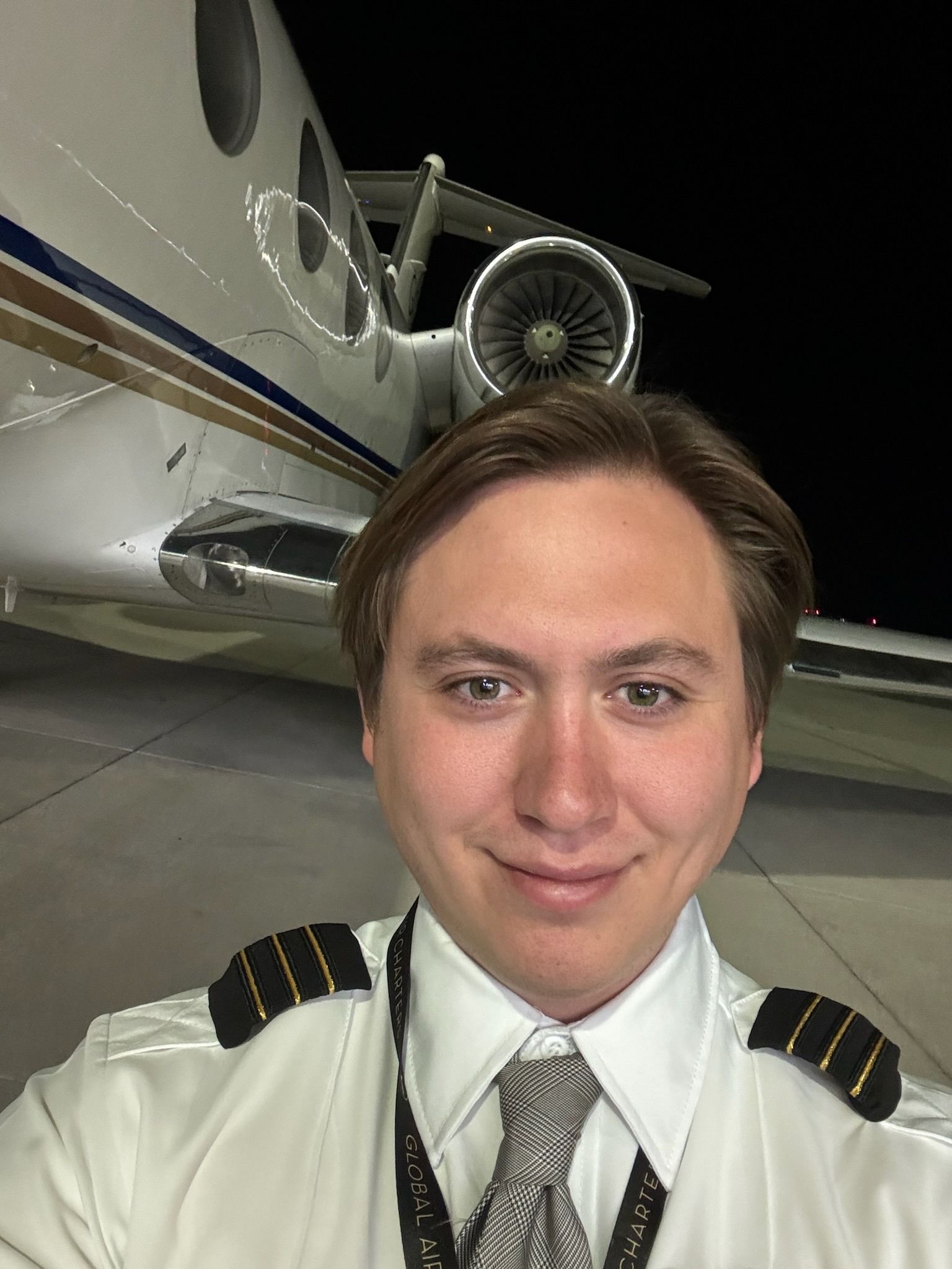 A man in a pilot 's uniform is taking a selfie in front of an airplane.