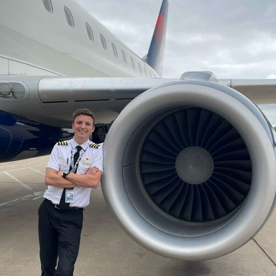 A man in a pilot 's uniform is standing in front of an airplane
