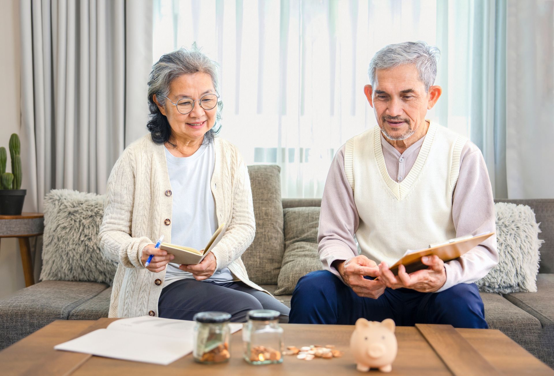 Two people sitting on a sofa, smiling and reading books in a bright living room