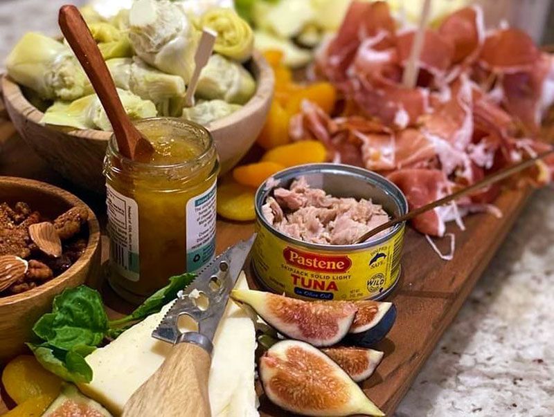 Charcuterie board with prosciutto, cheeses, olives, tuna, bread, and honey jar on a wooden platter