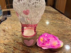Small decorative candle holder with pink heart accents beside a pink flower on a granite countertop