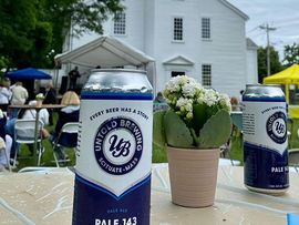 White farmhouse backyard party with beer cans, flowers, and guests seated at tables