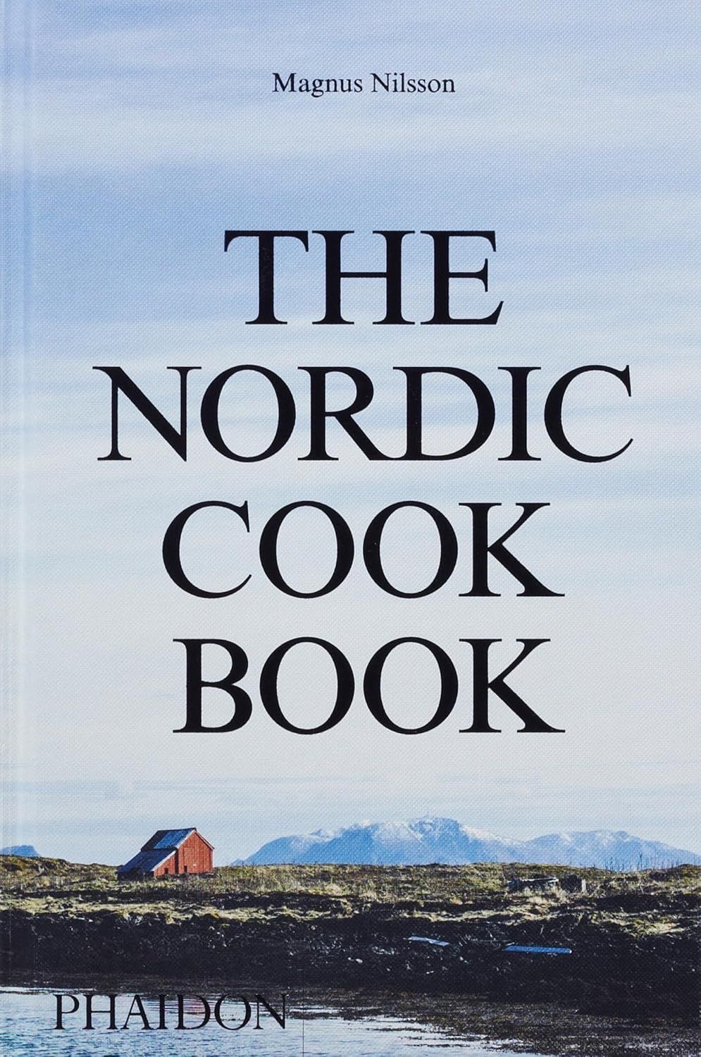 Book cover reading “The Nordic Cook Book” with a snowy coastal landscape and small red house.
