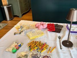 Craft supplies spread on a table with pencils, beads, stickers, and a desk lamp