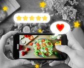 Hands holding a phone photographing a colorful salad with rating stars and a heart icon on screen