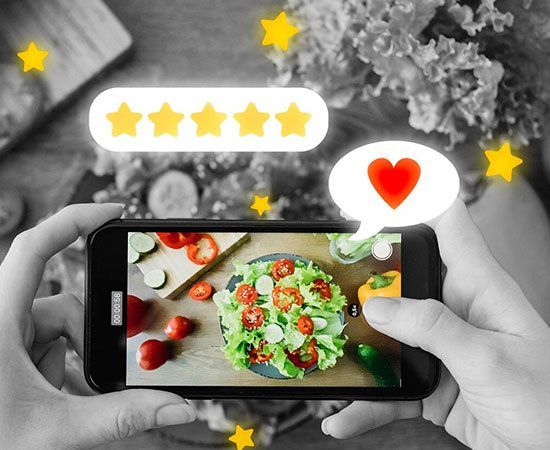 Hands holding a phone photographing a colorful salad with rating stars and a heart icon on screen