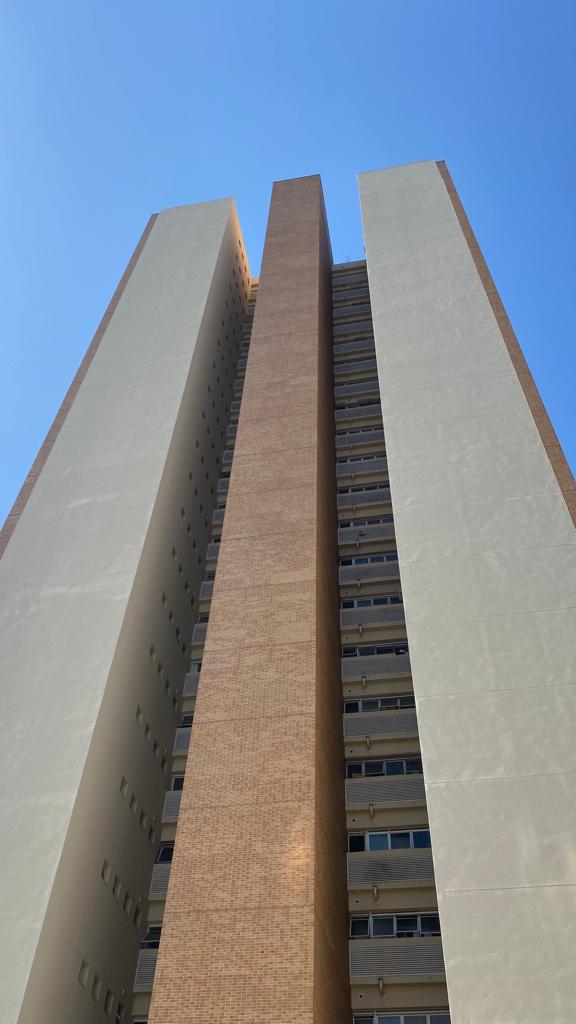 Olhando para um prédio alto com um céu azul ao fundo.