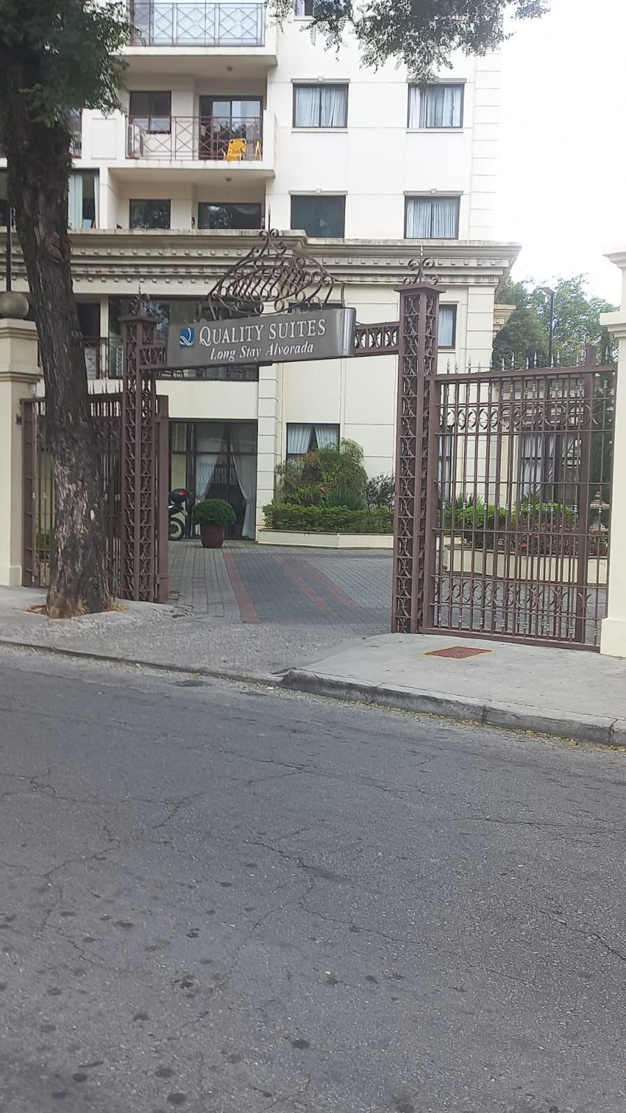 Um edifício com um portão que dá acesso a ele e uma árvore na frente dele.