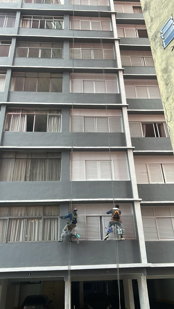 Dois homens estão pintando a lateral de um prédio alto.