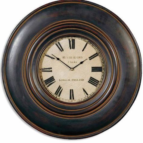 Round, dark-framed wall clock with Roman numerals, a cream-colored face, and the words 