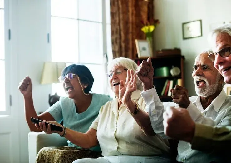 People sitting on a couch, smiling and cheering while watching TV in a bright living room