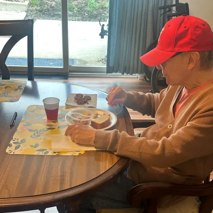 Person in a red cap eating at a dining table by a window.