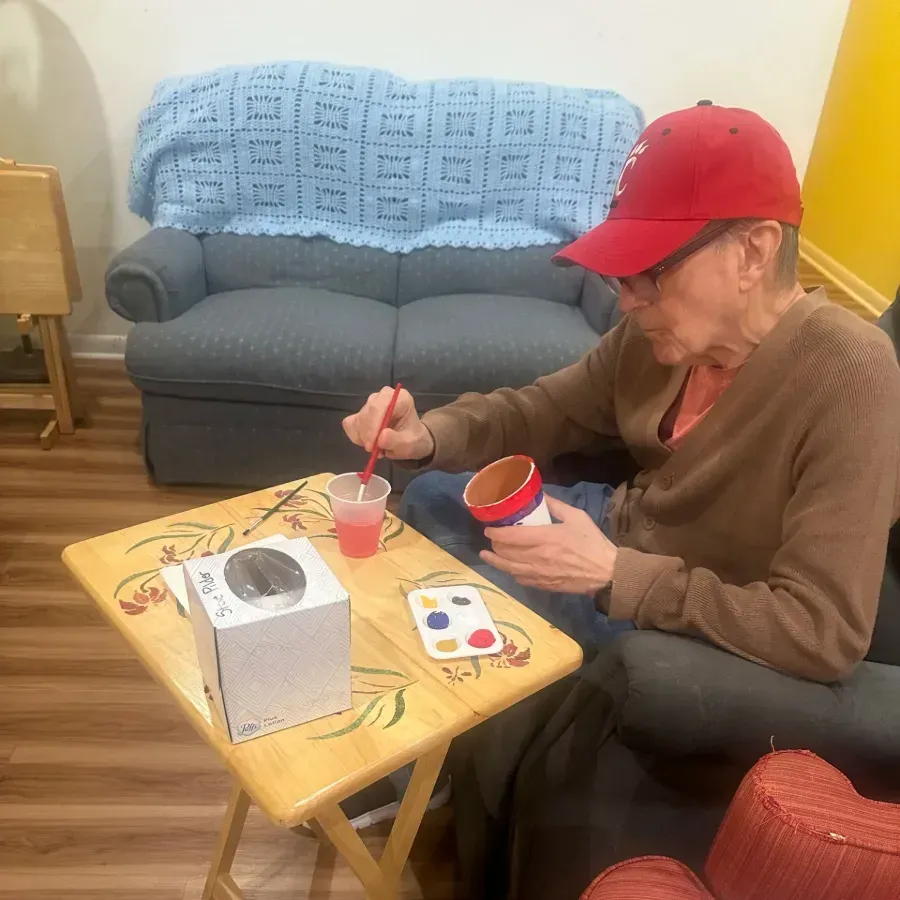 Person in red cap painting at a small table in a living room.