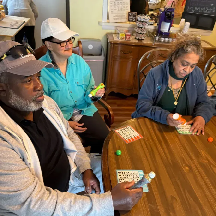 Two people playing a tabletop game in a living room, with cards on a small table and a red chair nearby.
