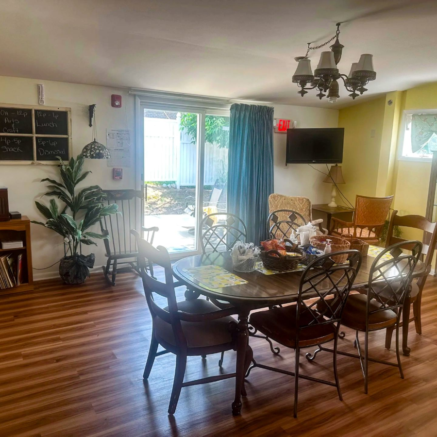 Bright dining room with glass table, wicker chairs, piano, plants, and sunlight through sliding doors