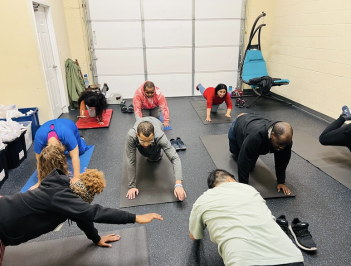 People exercising on yoga mats in a garage fitness class, doing plank stretches.