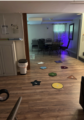 Indoor room with colorful floor markers leading to a table area under purple-blue lighting