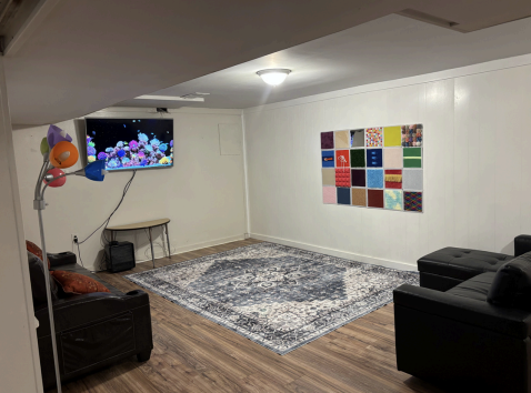 Basement living room with wall TV, patterned rug, black chairs, and colorful wall art