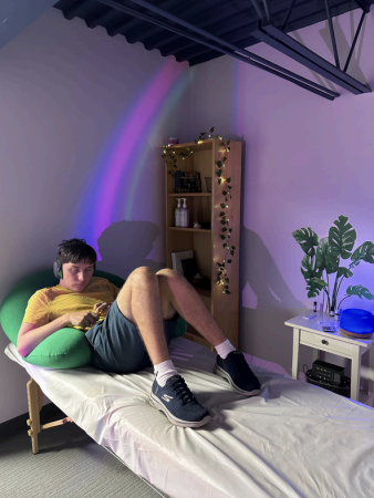 Person lounging on a bed in a softly lit room with purple accent lights and a small shelf of string lights.