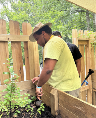 Man in yellow shirt and hat working on a wooden garden fence in a backyard