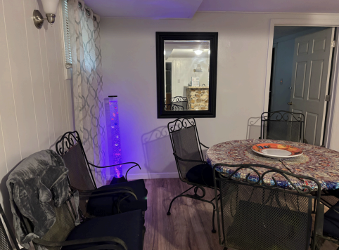 Dining area with glass table, black chairs, lit purple lamp, and wall mirror on hardwood floor