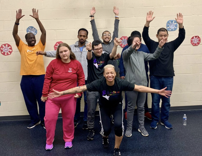 Group of people posing indoors with arms raised in a gym, smiling and celebrating together