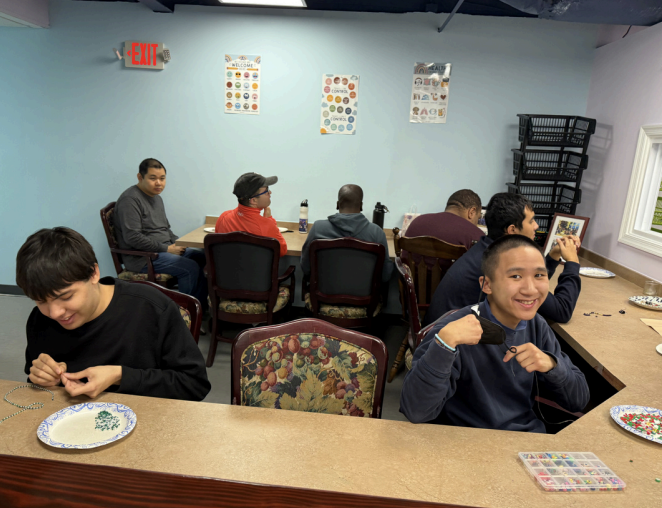 People seated in a community room, chatting and eating at tables, with posters on the wall.