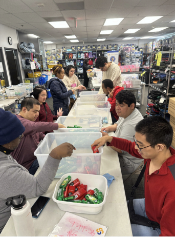 People sorting red and green items into bins at long tables in a bright indoor workshop