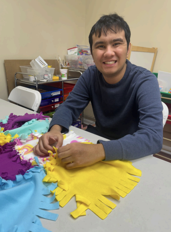 Person smiling at a table, arranging colorful paper crafts in a classroom or workshop setting.