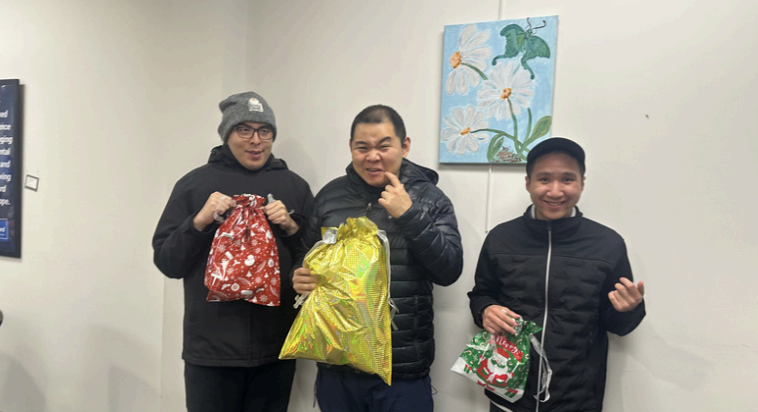 Three people standing indoors, each holding a wrapped gift bag and smiling for the camera.