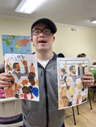 Person in a classroom holding two colorful collage art pieces while smiling at the camera