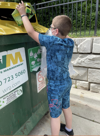 Child in blue outfit depositing items into a yellow-lidded recycling bin outdoors