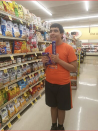 Person in an orange shirt holding a purple package in a grocery store aisle.