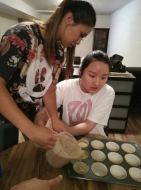 Two people pouring batter into muffin tins in a kitchen