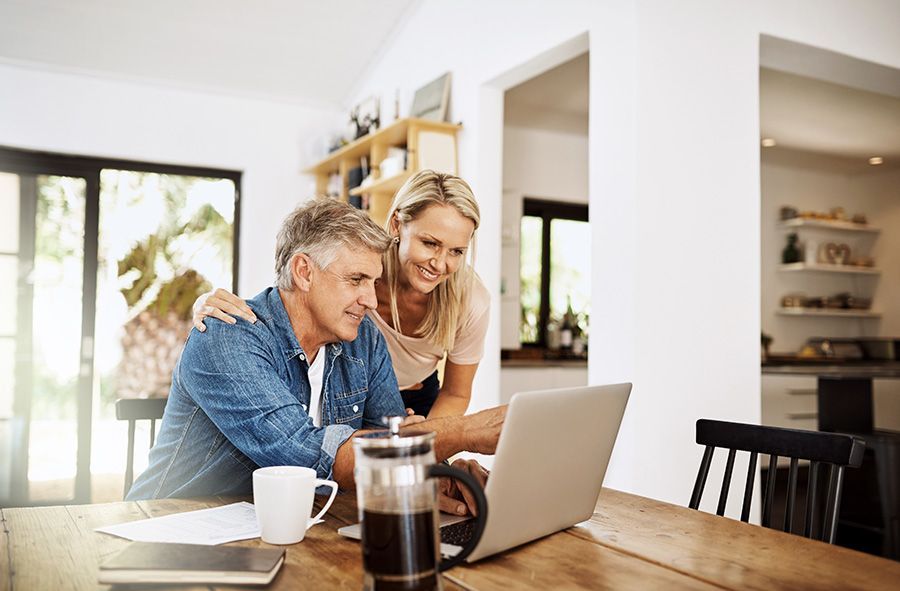 An elderly couple is sitting at a table with a laptop and a notebook.