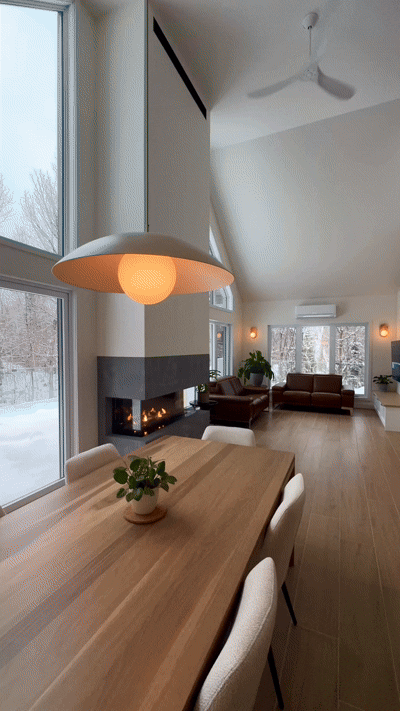 Une maison moderne aux tons clairs, avec des boiseries sombres et de grandes fenêtres, entourée de neige dans un cadre boisé.