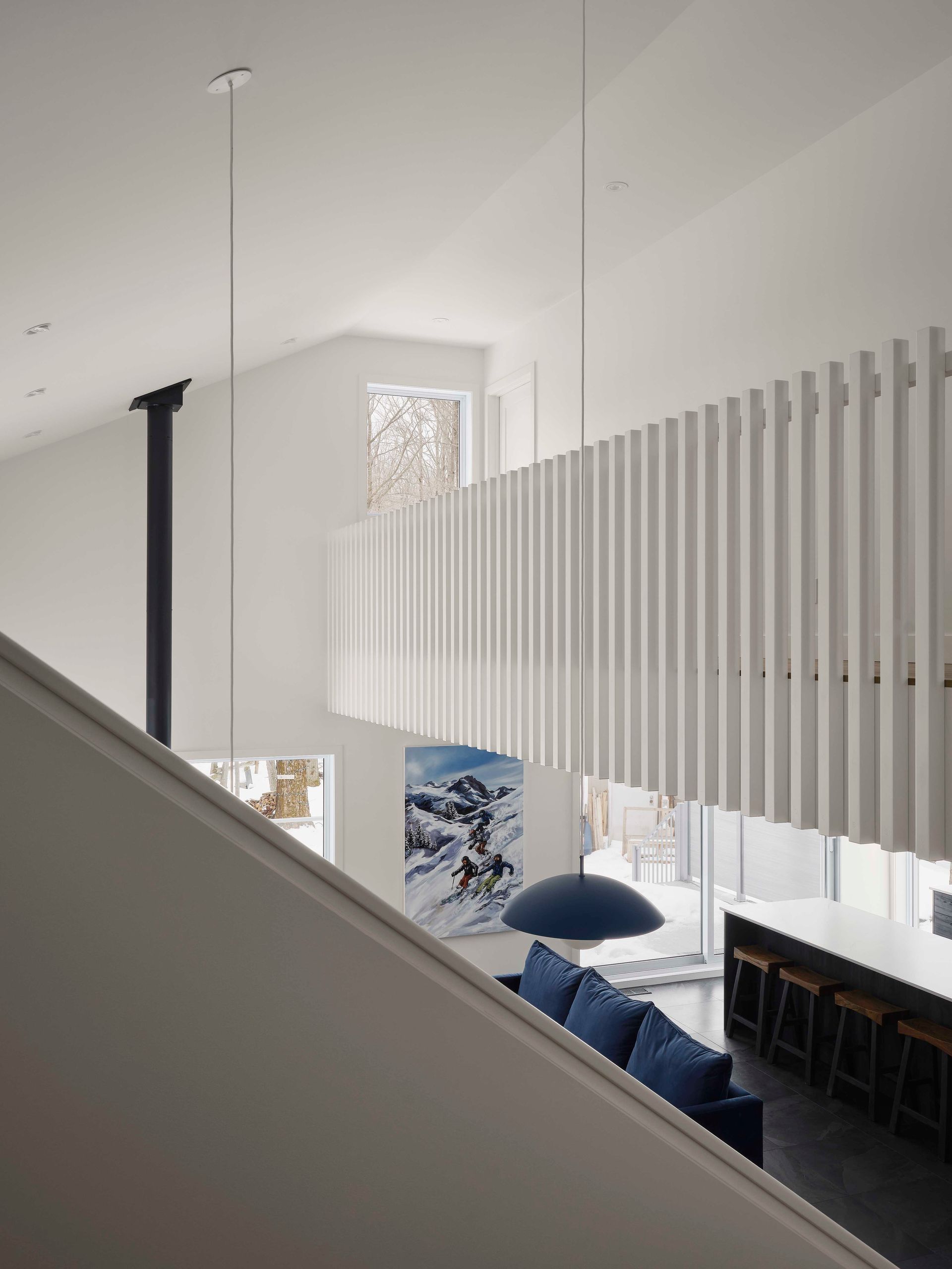 Un int&eacute;rieur lumineux et moderne comprend une balustrade de mezzanine blanche &agrave; lattes, un canap&eacute; bleu, un long comptoir et un plafond vo&ucirc;t&eacute;.