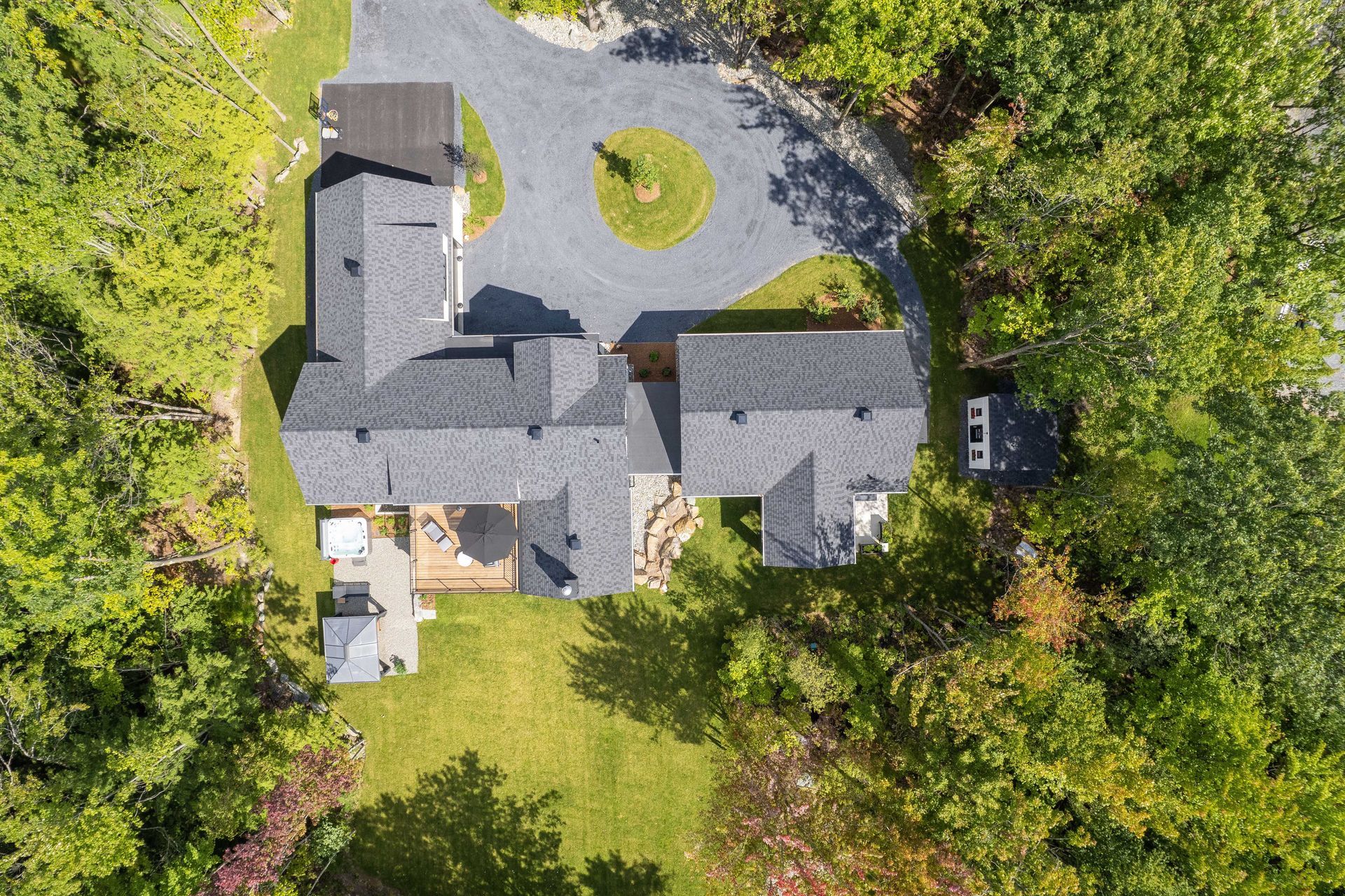 Vue a&eacute;rienne d'une maison au toit gris et &agrave; l'all&eacute;e circulaire en gravier, entour&eacute;e d'une for&ecirc;t verdoyante luxuriante.