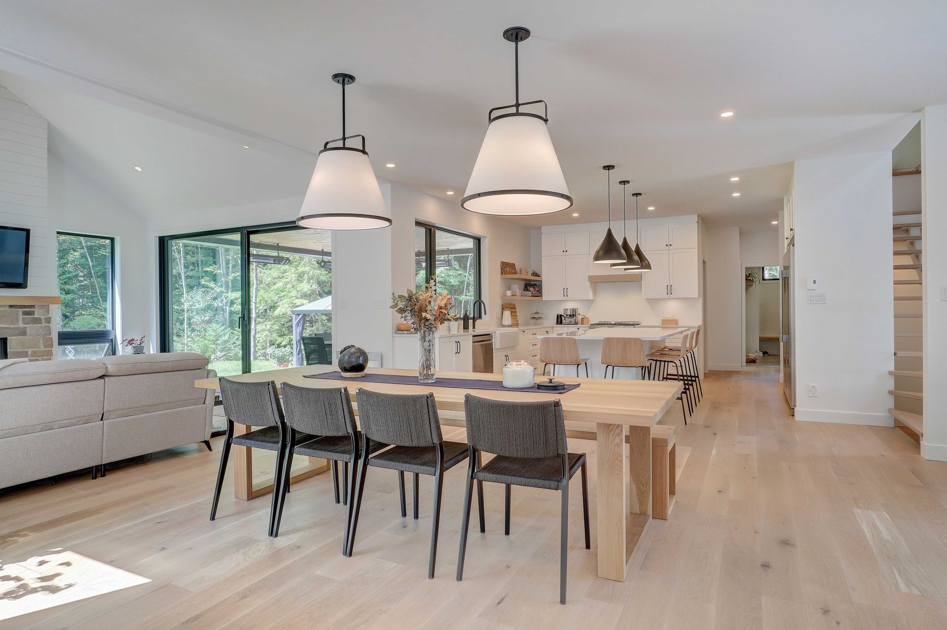 Une salle &agrave; manger lumineuse et moderne, &agrave; aire ouverte, avec une table en bois, six chaises et un &eacute;clairage suspendu contemporain.
