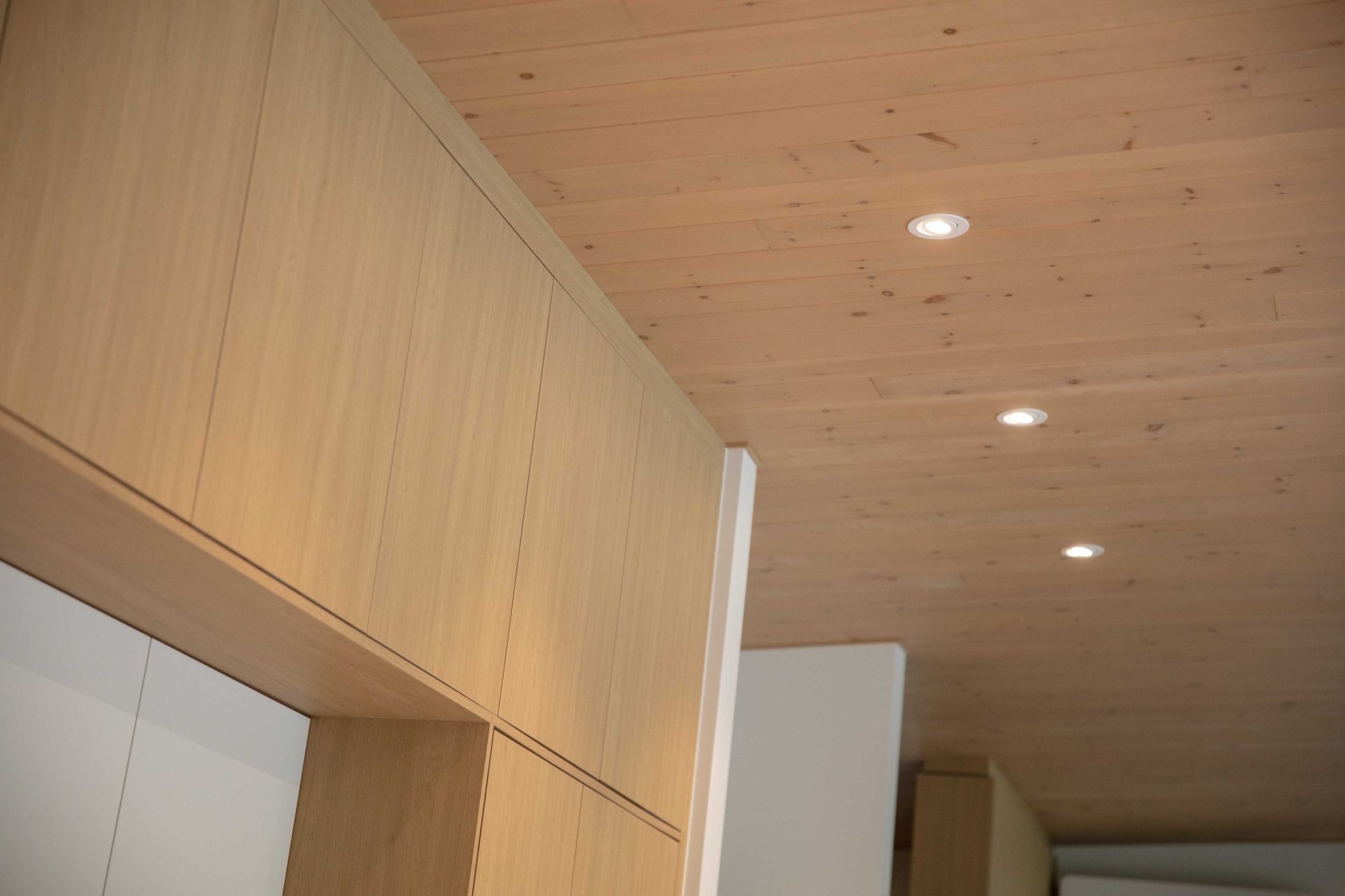 Dans un int&eacute;rieur moderne, un plafond lambriss&eacute; de bois clair avec trois spots encastr&eacute;s surplombe des meubles en bois clair.