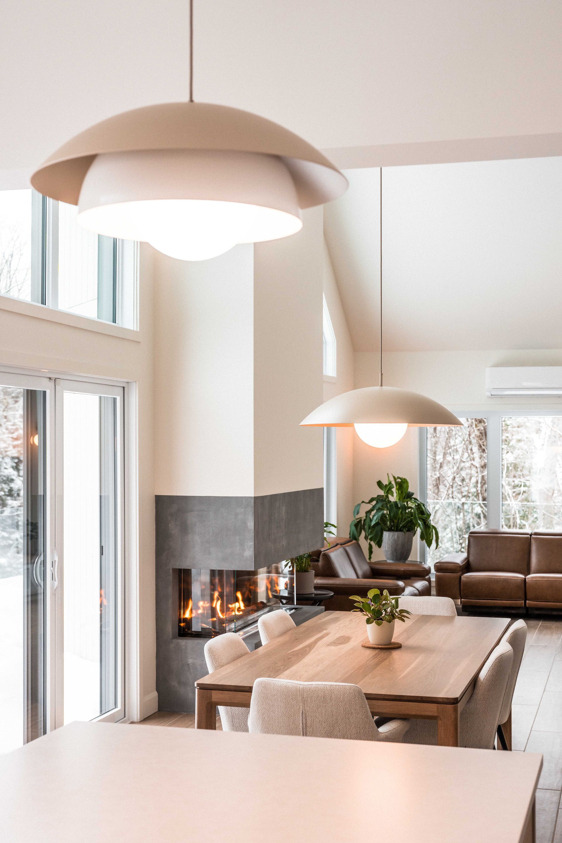 Deux suspensions en forme de d&ocirc;me surplombent une table &agrave; manger en bois dans un espace de vie moderne et lumineux agr&eacute;ment&eacute; d'une chemin&eacute;e d'angle.