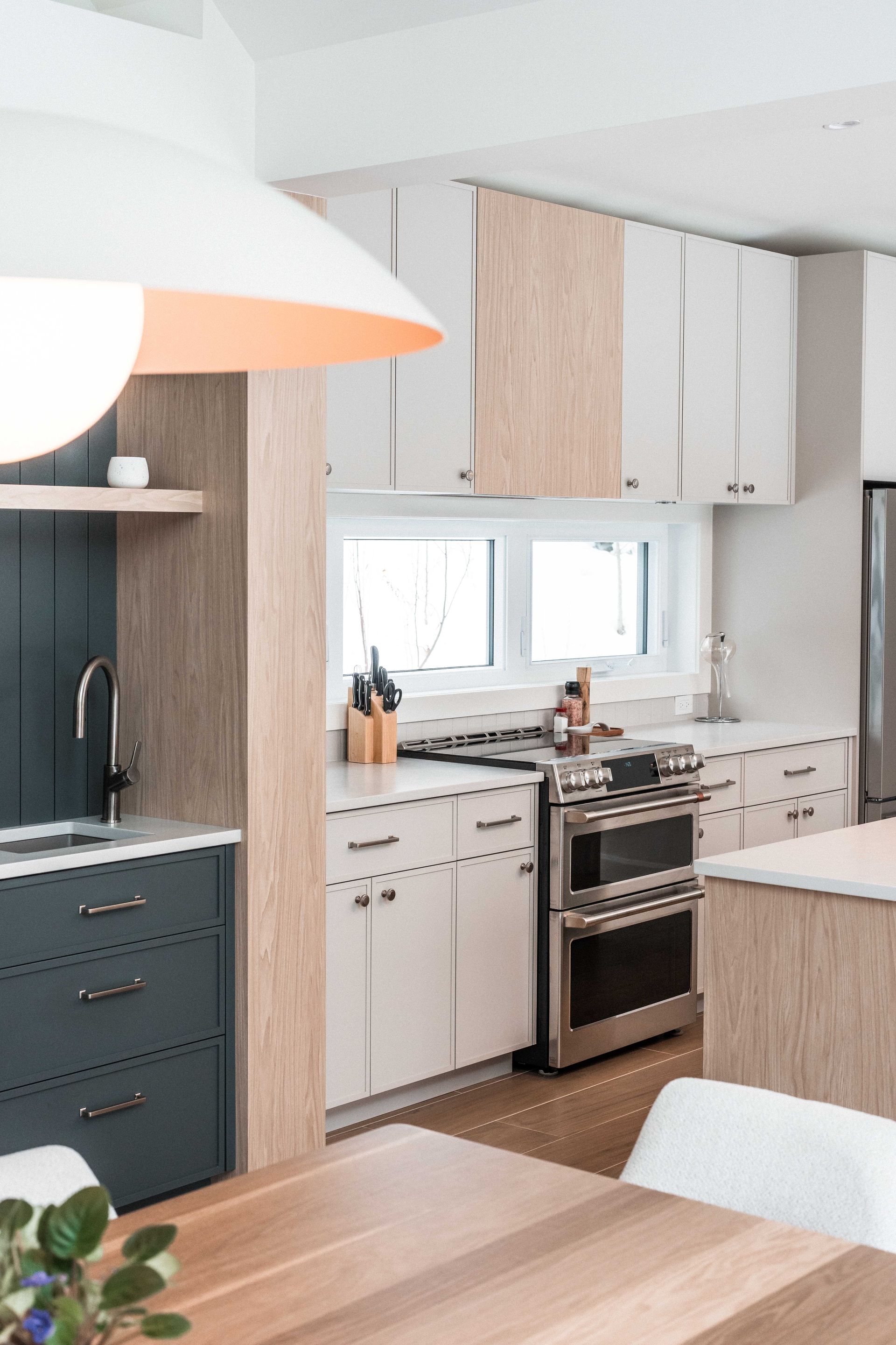 Une cuisine moderne avec des armoires blanches et en bois naturel, un &icirc;lot bleu fonc&eacute;, une cuisini&egrave;re en acier inoxydable et un parquet.