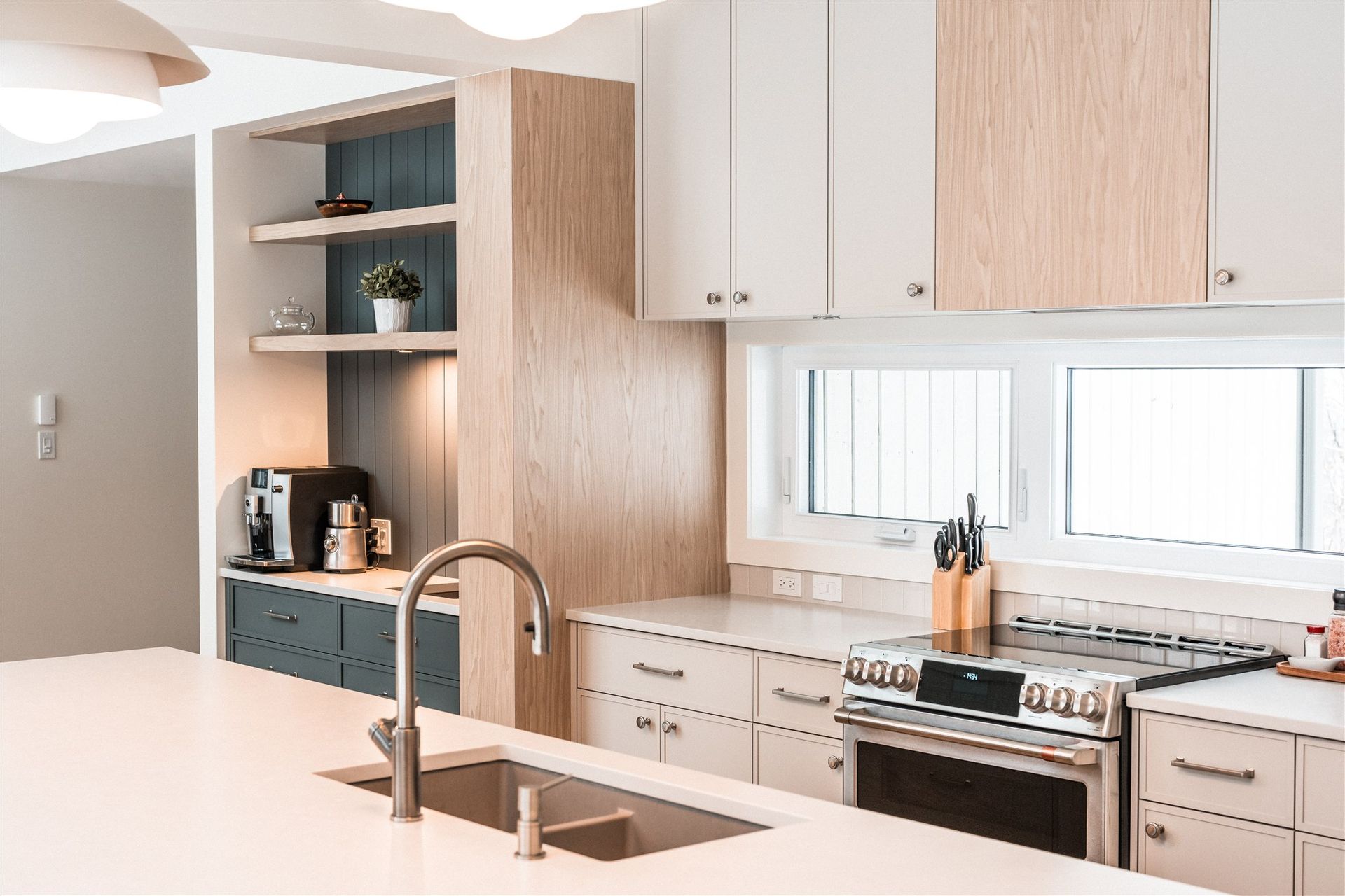 A modern kitchen with light wood accents, white cabinetry, a large center island, stainless steel stove, and open shelving.