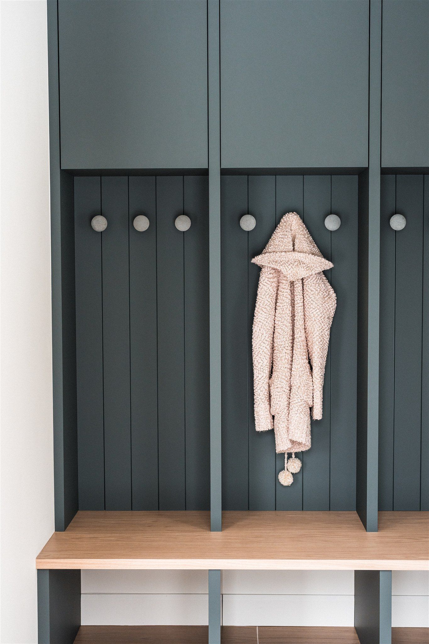 Un meuble de rangement en bois bleu foncé avec des crochets, un banc en bois clair et un pull crème suspendu.
