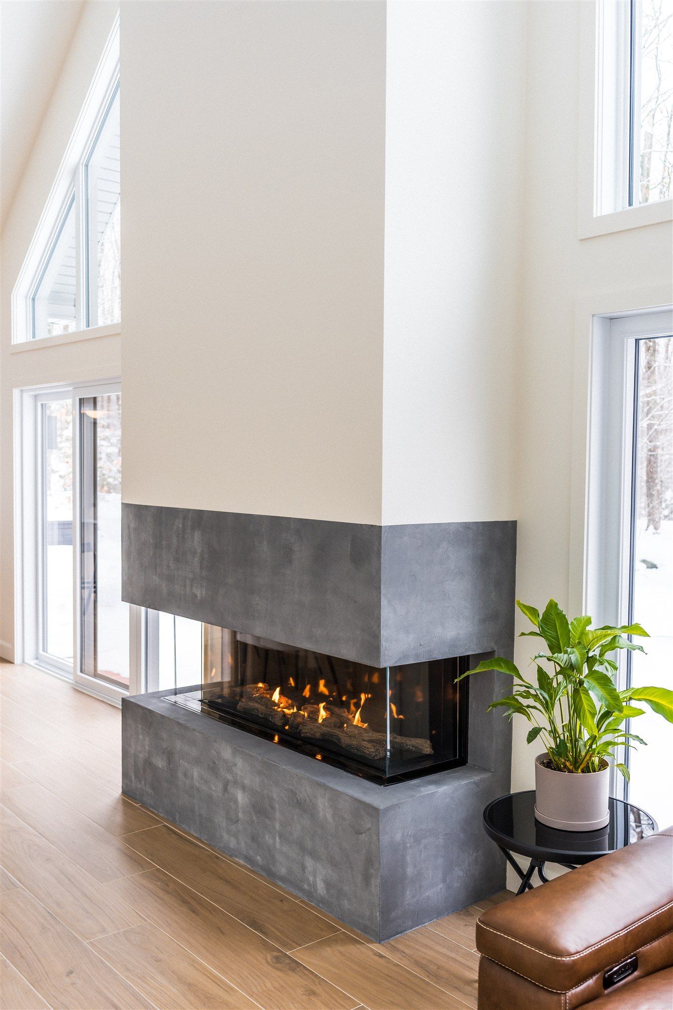 Une cheminée moderne avec une partie supérieure blanche et une base en pierre grise, installée dans une pièce avec de grandes fenêtres et un parquet en bois dur.
