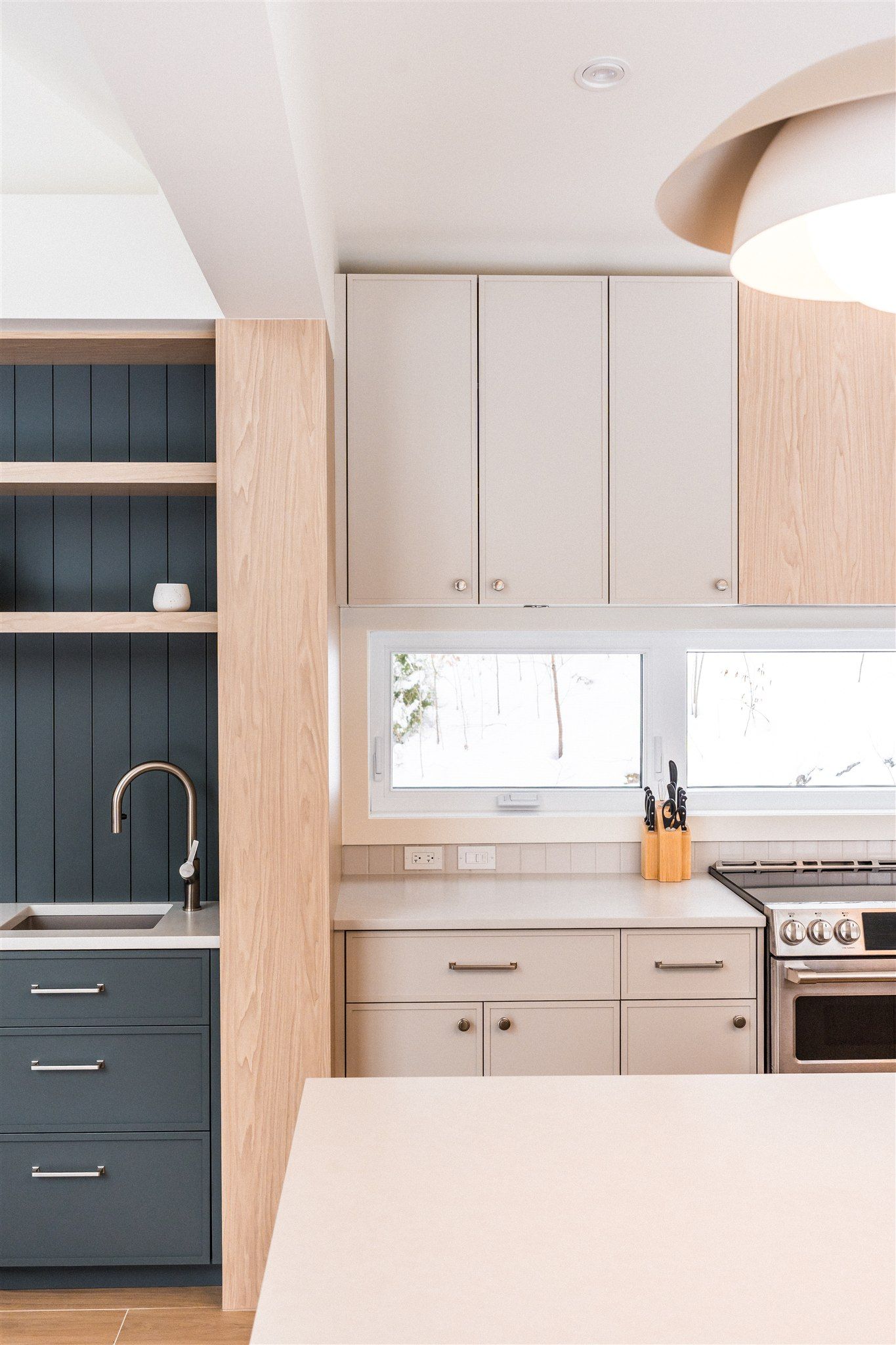 Une cuisine moderne avec un évier bleu foncé encadré de bois, des placards clairs, un plan de travail blanc et une cuisinière.