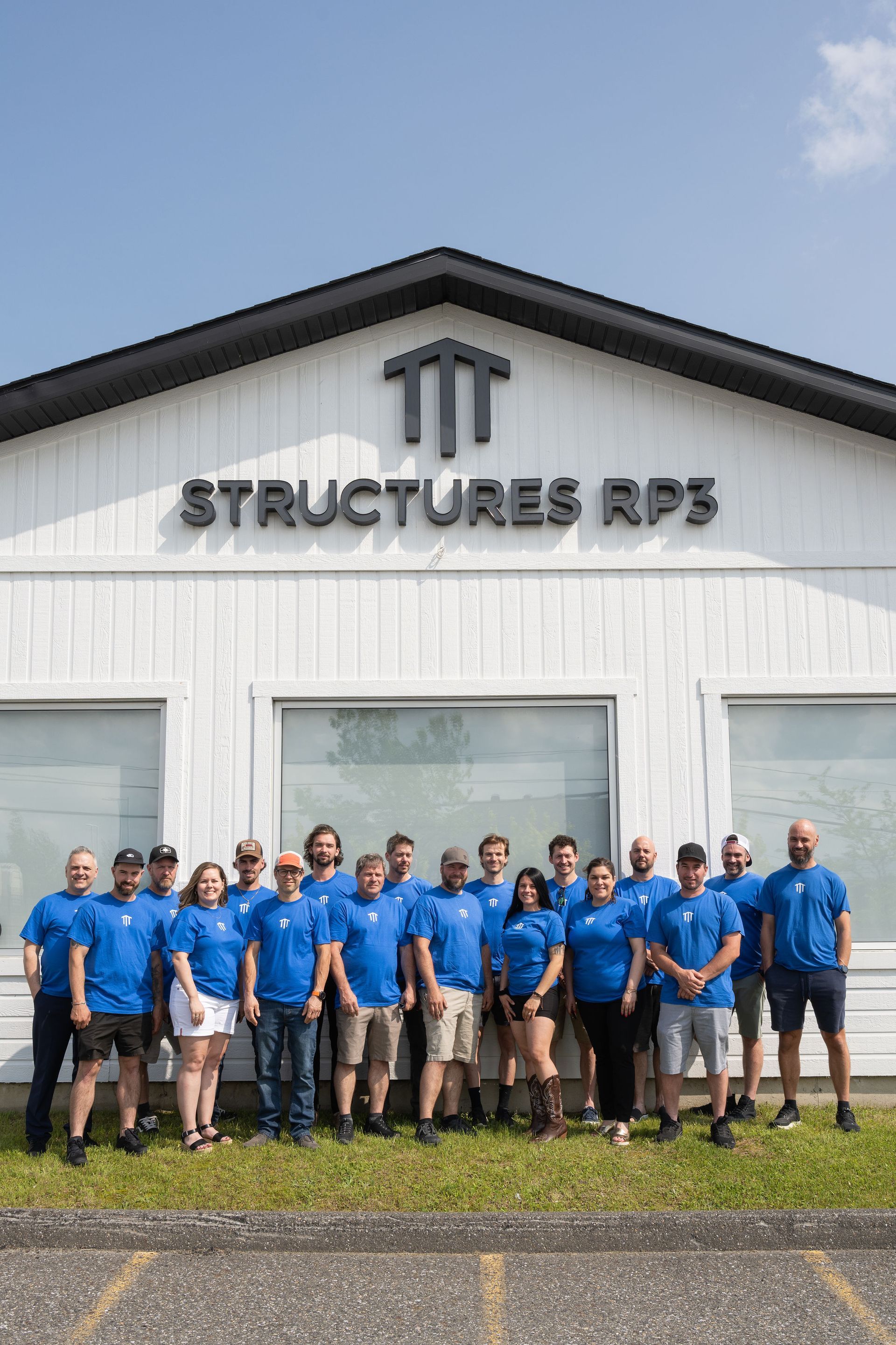 A group of people wearing blue shirts stands outside a white building labeled