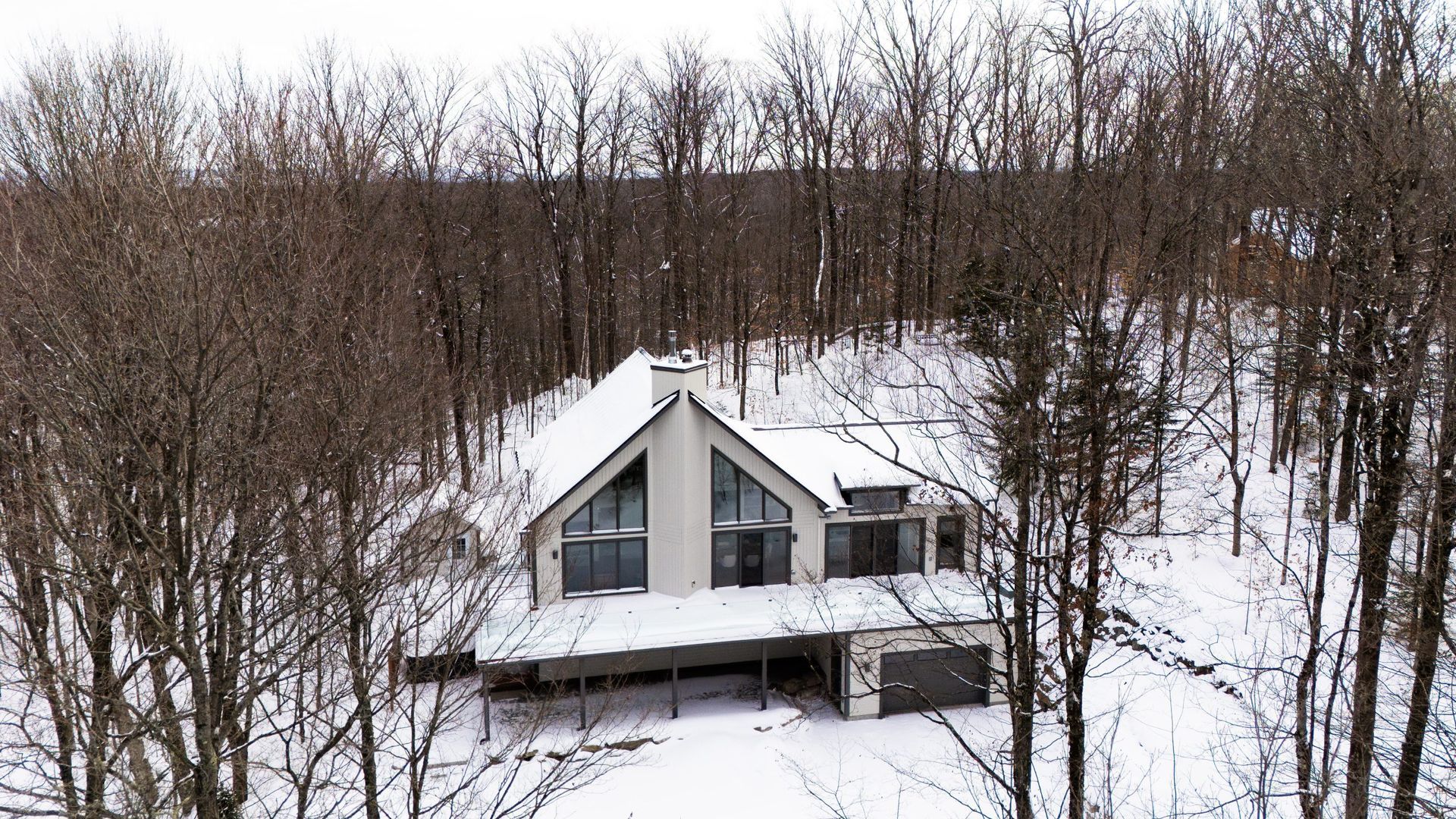 Une maison blanche en forme de A nichée dans une forêt enneigée en hiver.